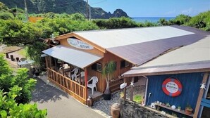 A building with a covered outdoor seating area, a sign with Japanese characters, and a view of the ocean. - House Hotel Amami Minpaku Mura & Sauna (Amami)