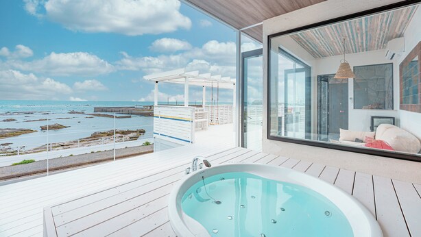 Un espace moderne aménagé à l’extérieur, avec un jacuzzi et une vue sur la mer et le littoral rocheux.