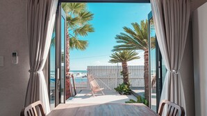Ein Balkon mit Holztisch und Stühlen, Blick auf den Strand, Palmen und ein weißer Zaun.