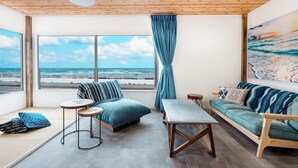 Un salon moderne doté d’une grande fenêtre donnant sur l’océan, d’un plafond en bois et d’un coin salon confortable avec un canapé et une table.