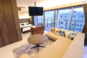 Une chambre d’hôtel avec un lit, un canapé, une petite table, une télévision et un balcon donnant sur la ville.