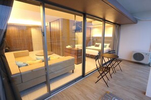 Une chambre d’hôtel moderne avec une cloison en verre, un canapé, une petite table et un lit.