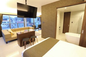 Une chambre d’hôtel moderne dotée d’un grand lit, d’un bureau avec deux chaises, d’un canapé, d’une télévision et d’une salle de bain avec baignoire.