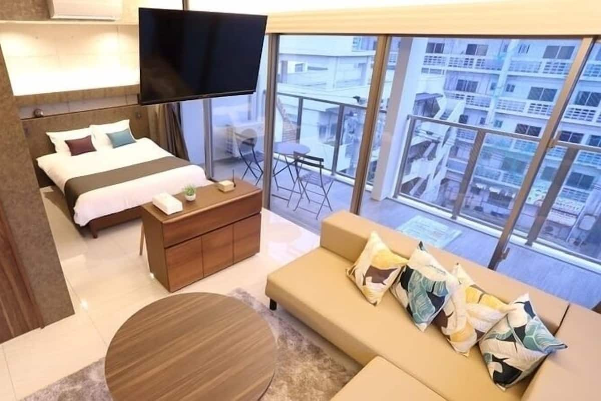 Ein modernes Hotelzimmer mit einem großen Bett, einer Sitzecke, einem Fernseher und einem Balkon mit Blick auf die Stadt.