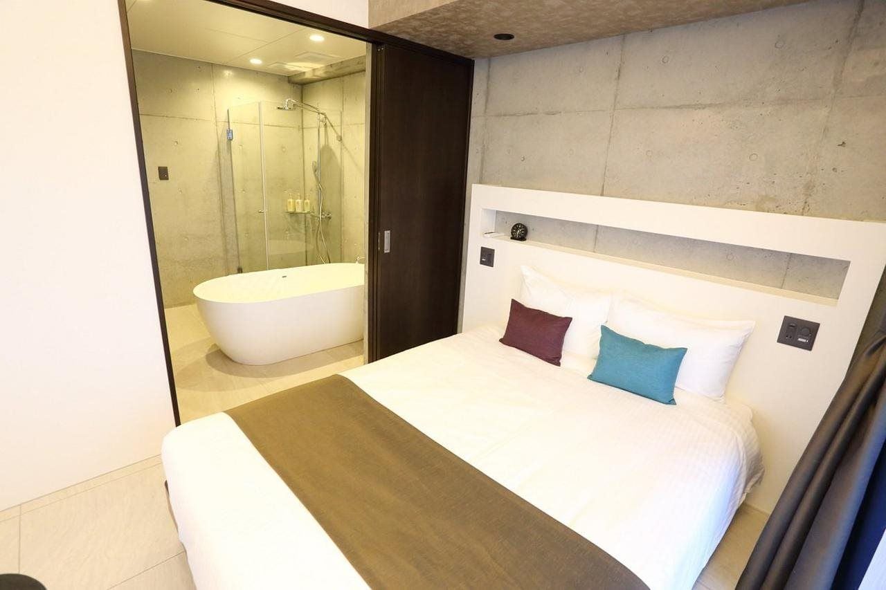 A modern hotel room with a large bed, a separate bathroom with a bathtub, and a glass shower enclosure.