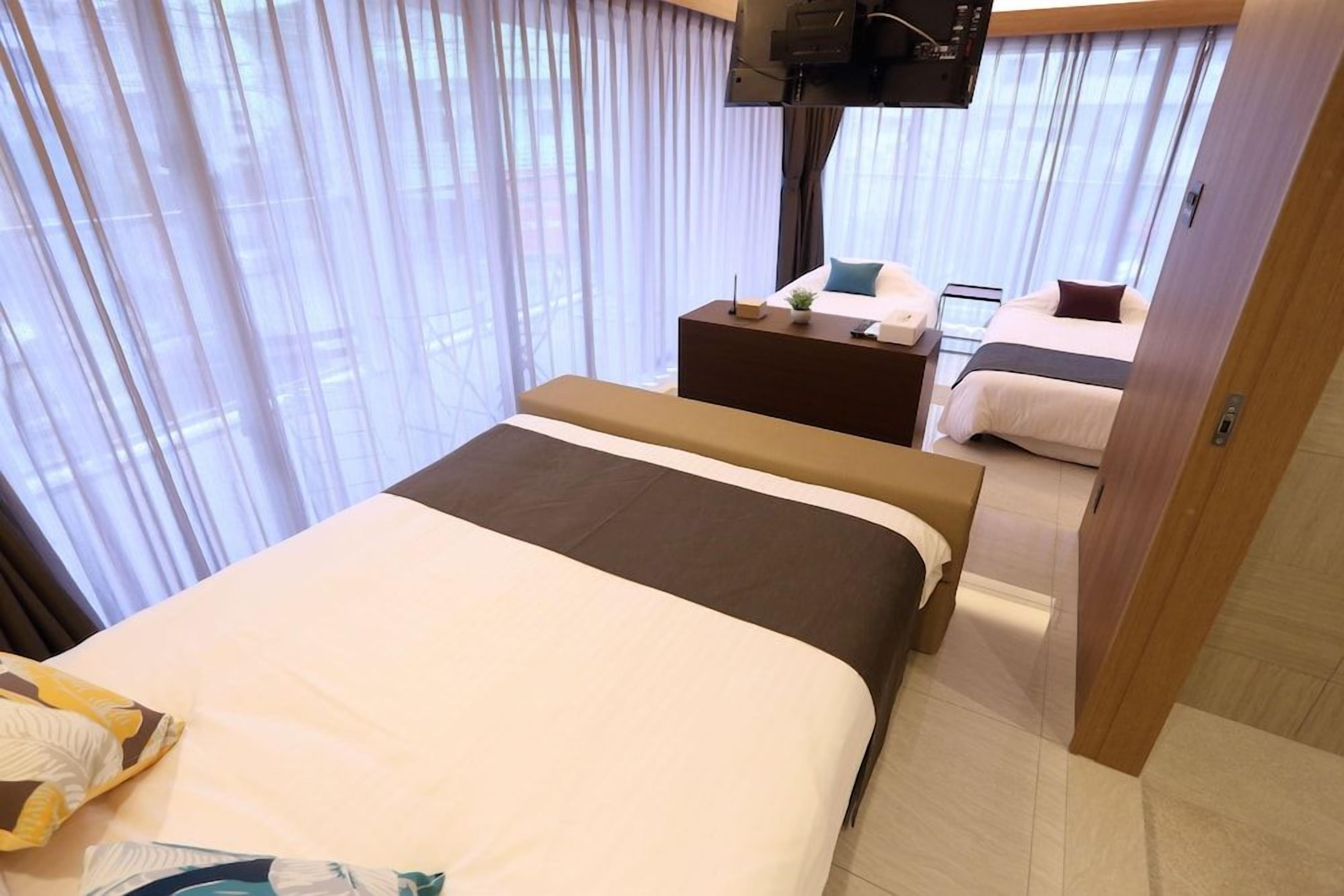 A hotel room with a bed, a bedside table, a TV, and a window with curtains.