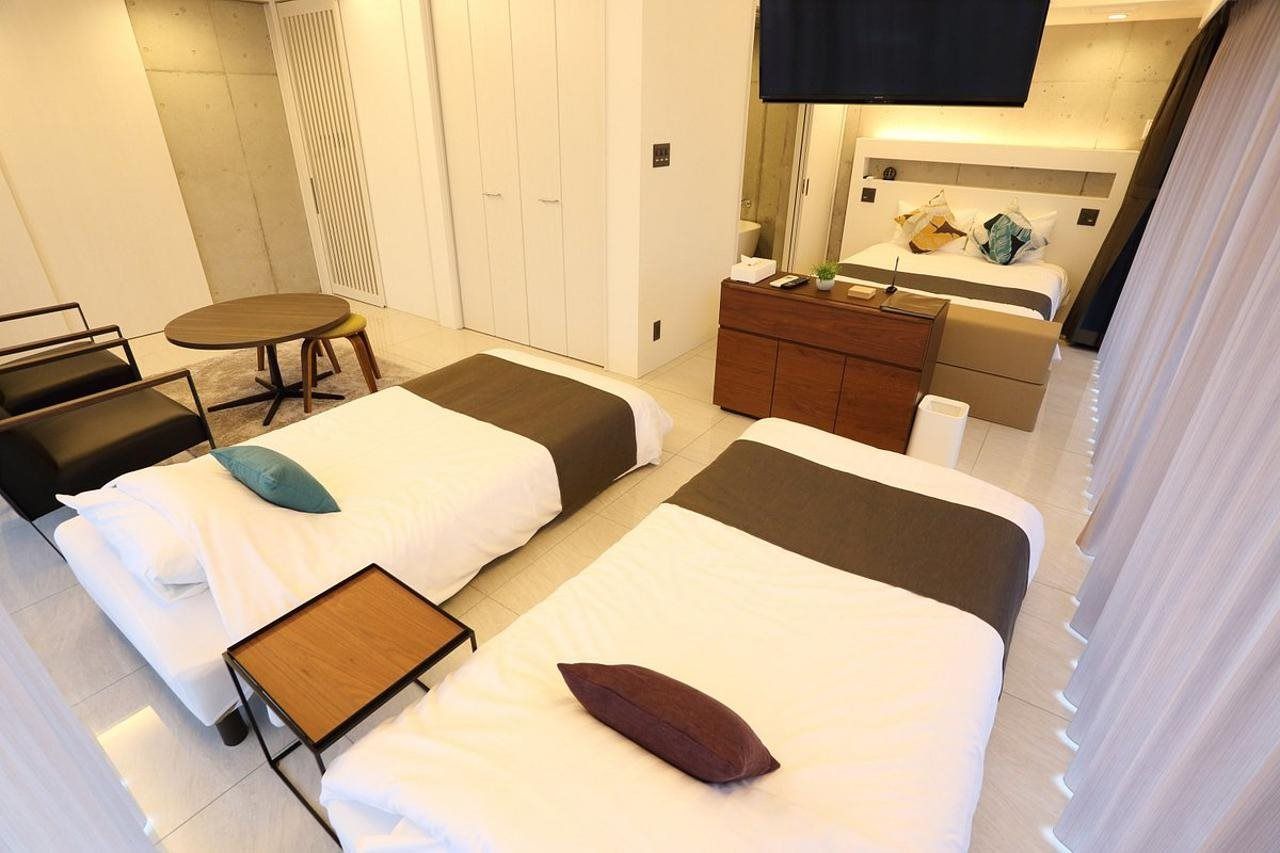 A hotel room with two beds, a small table, a sofa, a TV, and a wardrobe.