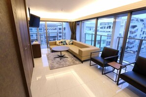Ein modernes Wohnzimmer mit einer Couch, einem runden Couchtisch und zwei Sesseln. Große Fenster bieten Blick auf die Stadtlandschaft.