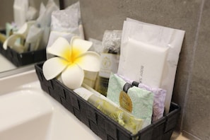 Ein Badezimmer mit einem schwarzen Korbwäscheskorb, der Toilettenartikel, eine weiße Blume und ein Badesalzfläschchen enthält.