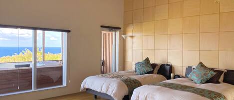A bedroom with two beds, a ceiling fan, a large window with a view of the sea, and a floor lamp.