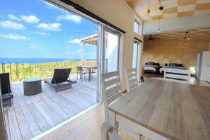 Une terrasse en bois avec des sièges d’extérieur, une grande table et une vue sur l’océan.