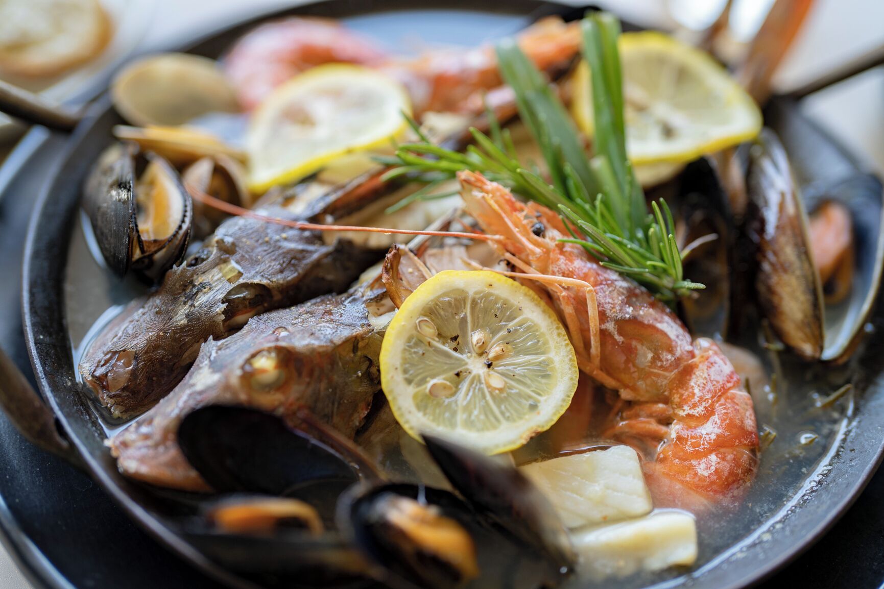 A seafood dish with mussels, shrimp, and fish, garnished with lemon and rosemary.