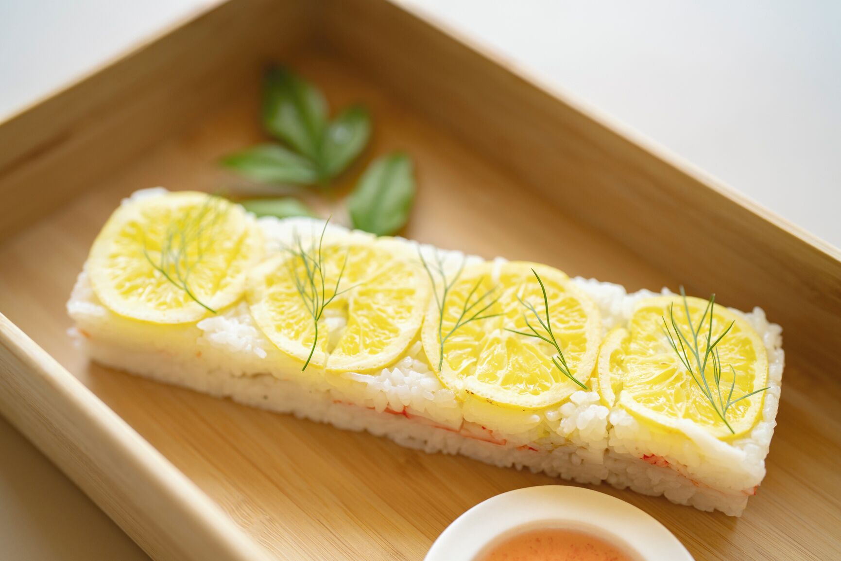 Un plato de sushi con rodajas de limón y adorno de eneldo sobre una bandeja de madera.