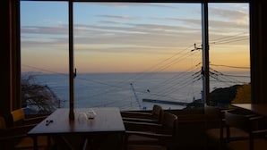 Un coin repas avec une table et des chaises, offrant une vue panoramique sur la mer et les lignes électriques au coucher du soleil.