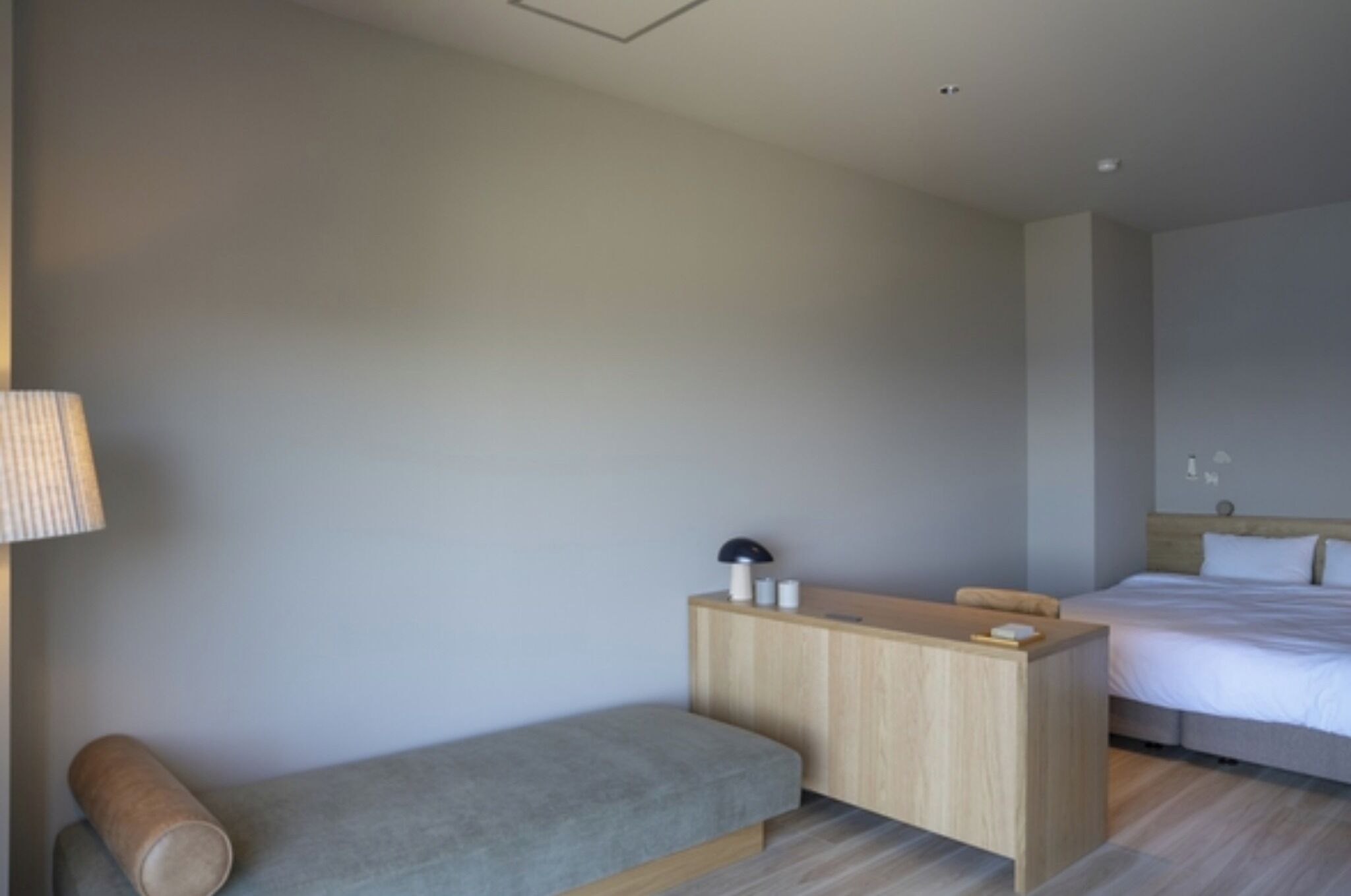 A hotel room with a bed, a desk, a lamp, and a bench.