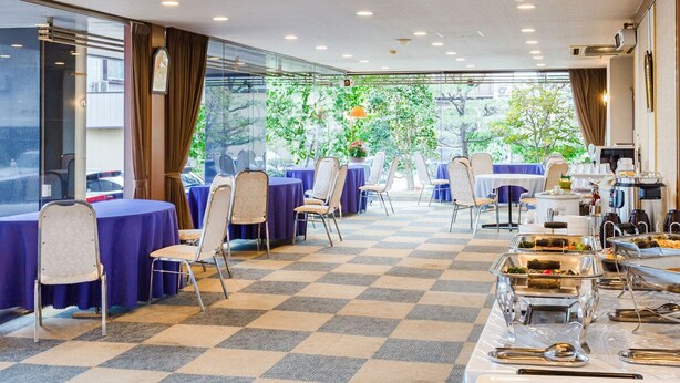Un salón de banquetes con mesas redondas cubiertas con manteles azules, sillas y estaciones de buffet con comida.