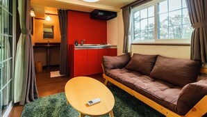 A compact living space with a sofa, a small table, a kitchenette, and a window with curtains. - Pica Fuji Grinpa (Susono)