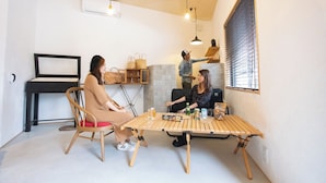 A room with a wooden table, chairs, a piano, and a window with blinds. - Life Style Hotel Ichi (Kochi)