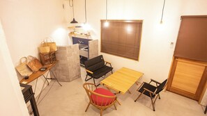 A compact living space with a wooden dining table, two chairs, a cushioned chair, a small kitchen area, and a window with blinds. - Life Style Hotel Ichi (Kochi)