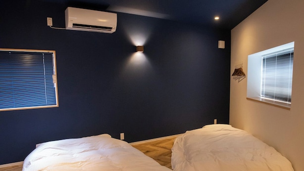 A bedroom with two beds, wooden flooring, a dark wall, and an air conditioning unit. - Life Style Hotel Ichi (Kochi)