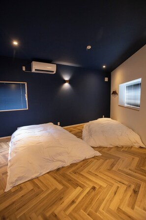A bedroom with two beds, wooden flooring, a dark wall, and an air conditioning unit. - Life Style Hotel Ichi (Kochi)
