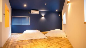 A room with a herringbone wooden floor, two white beds, a window with blinds, and an air conditioning unit on the wall. - Life Style Hotel Ichi (Kochi)