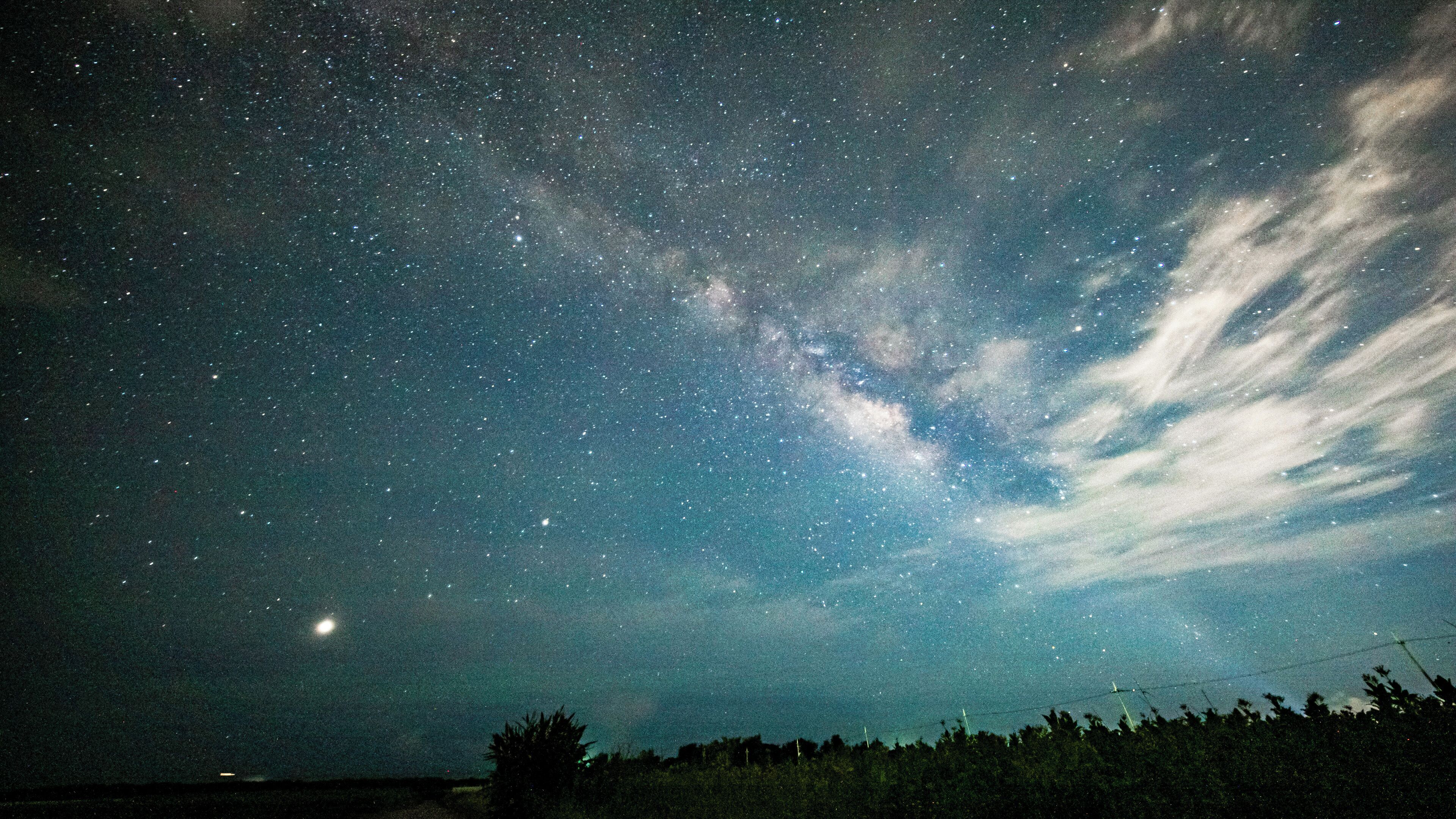 A starry night sky with visible clouds and a crescent moon.