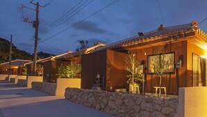 A row of traditional-style buildings with stone walls and tiled roofs, connected by overhead power lines. - Rereso Okinawa Churaumi (Motobu)