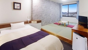 A hotel room with a bed, a desk, a TV, a window with a view, and a small table with a cushion. - Sasebo Daiichi Hotel (Sasebo)