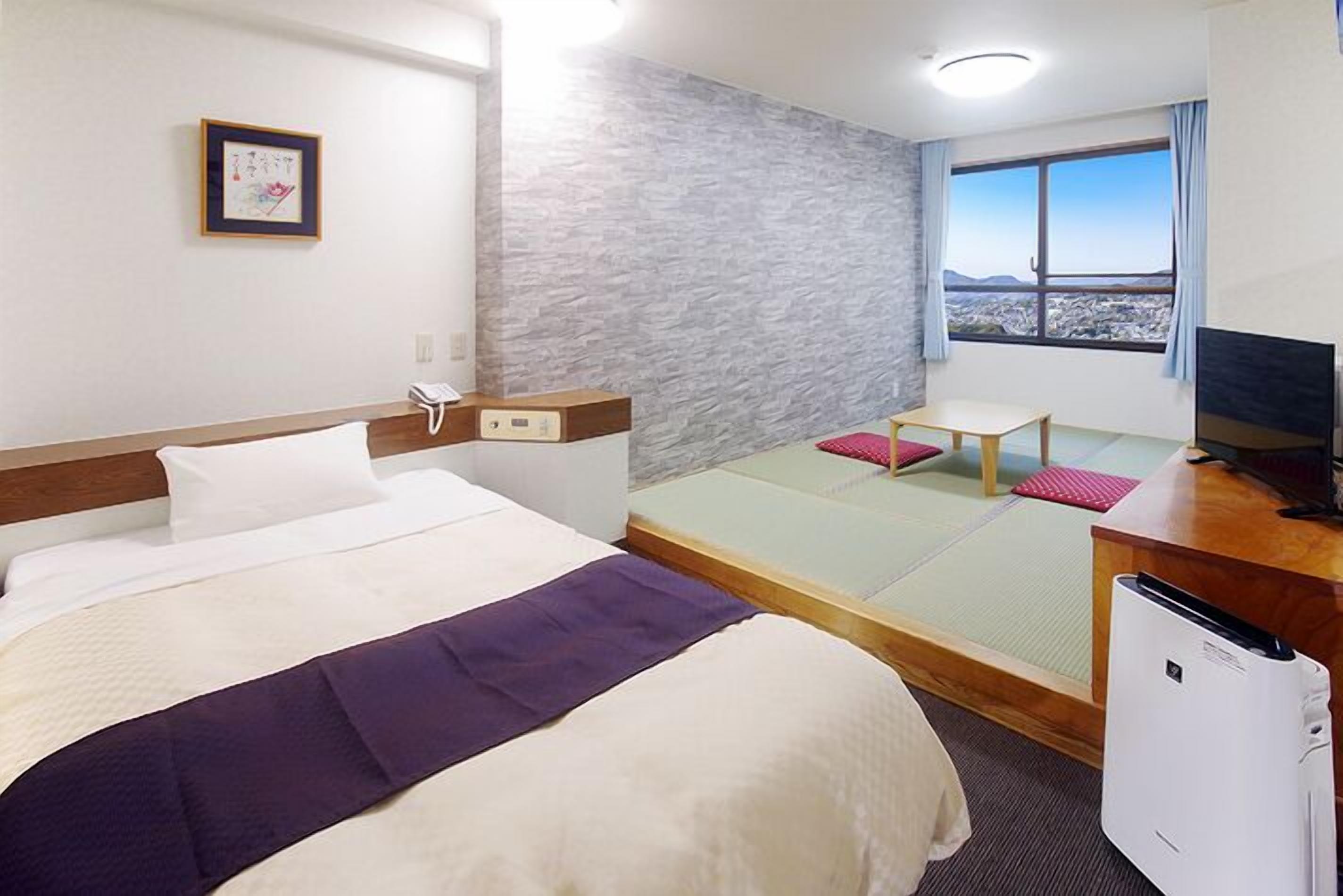 Une chambre d’hôtel équipée d’un lit, d’un bureau, d’une chaise, d’une télévision et d’une fenêtre donnant sur un paysage agréable.