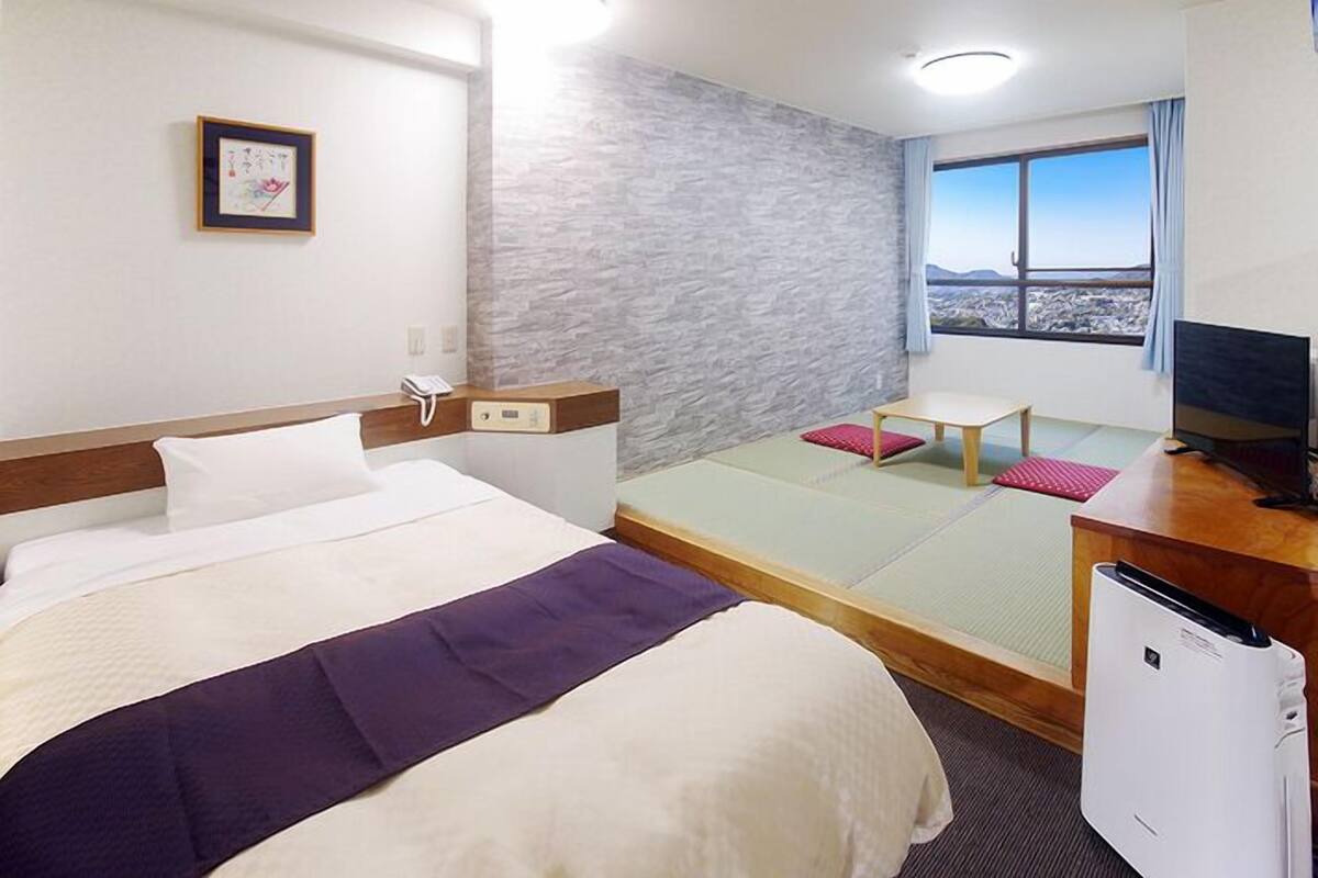 Une chambre d’hôtel équipée d’un lit, d’un bureau, d’une chaise, d’une télévision et d’une fenêtre donnant sur un paysage agréable.