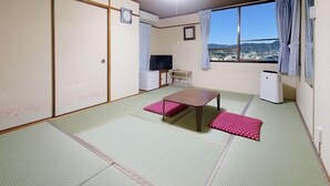 A traditional Japanese room with tatami flooring, a low table, and a view of a cityscape through large windows. - Sasebo Daiichi Hotel (Sasebo)