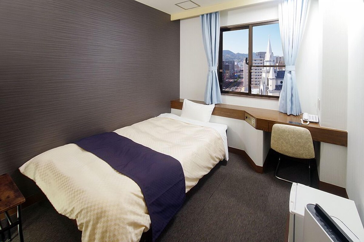 A hotel room with a bed, a desk, a chair, and a window with a city view.