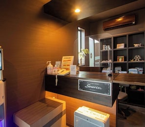 A reception desk with a sign reading 'Sourin' in a hotel lobby with wooden walls, a reception counter, a small plant, and a shelf with various items. - Oita Onsen Business Resort Sourin (Oita)