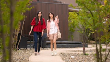 Two individuals walking on a pathway surrounded by trees and a building in the background.