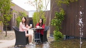 Two people seated at a table outdoors with a water feature in the background. - Oita Onsen Business Resort Sourin (Oita)