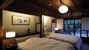 A traditional Japanese room with two beds, a wooden ceiling, and a large window with a view of greenery. - Kominkano Yado Saika-an (Maizuru)