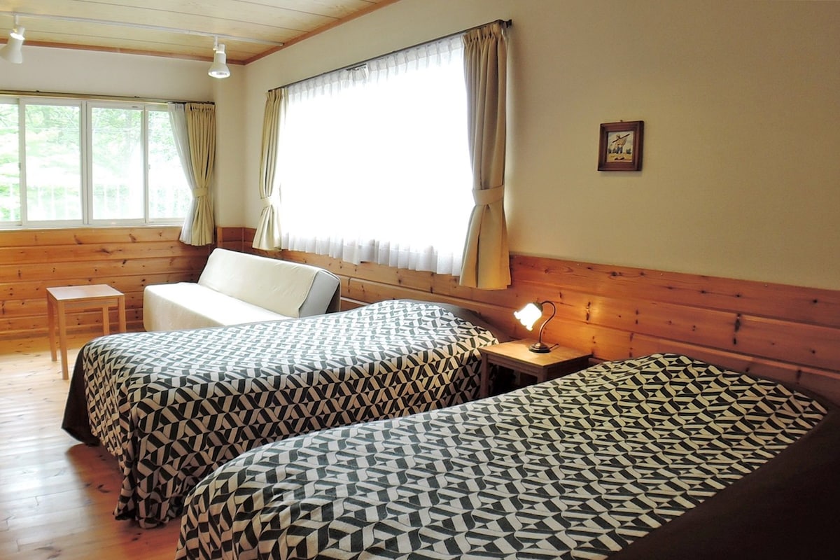 A room with two beds, a sofa, a small table, and a window with curtains.