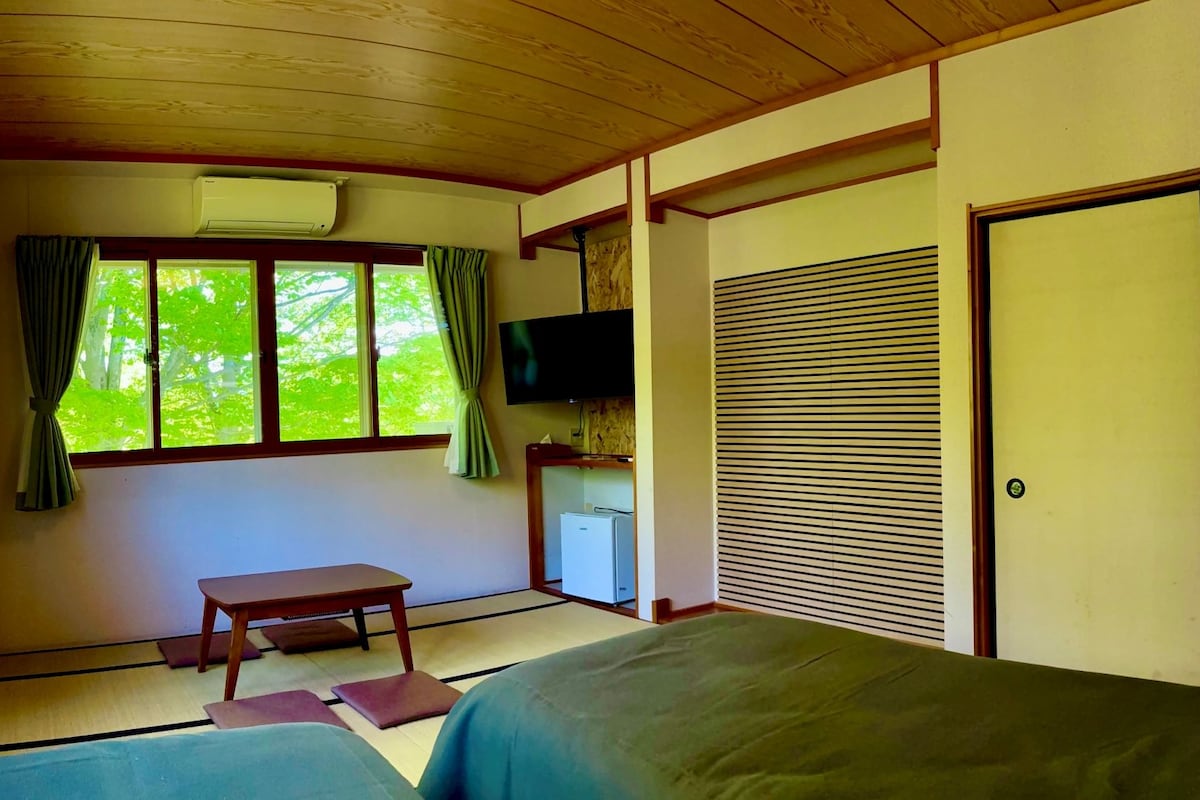 A room with tatami flooring, a bed, a table, a television, and a sliding door.
