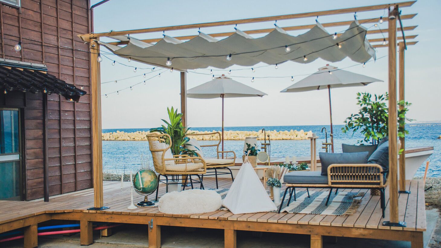 Una terraza de madera con mobiliario exterior, sombrillas y vistas al mar.