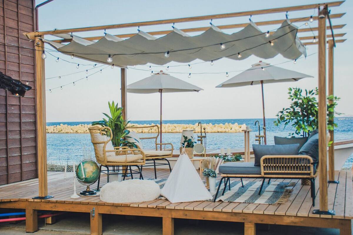A wooden deck with outdoor seating, umbrellas, and a view of the sea.