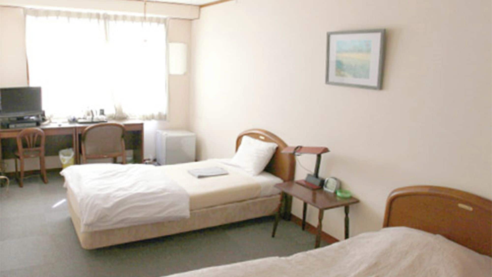 Una habitación de hotel con cama, escritorio, silla, televisión y mesita de noche con lámpara.