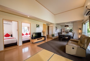 A modern living room with a sofa, a dining area, and a bedroom with a TV.