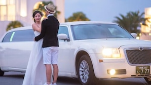 A couple embracing in front of a white luxury car with a license plate visible. - United Resort Kibogaoka (Onna)