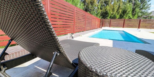 A poolside area with a red fence, a pool, and wicker furniture.