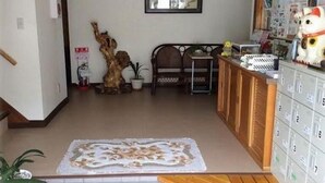 Una habitación con piso de madera, un escritorio, una silla, un aparador con cajones, una planta en maceta y una escultura de árbol decorativa.