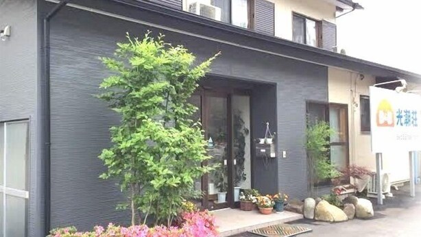 Un edificio de fachada oscura, un pequeño árbol y plantas en macetas al frente.