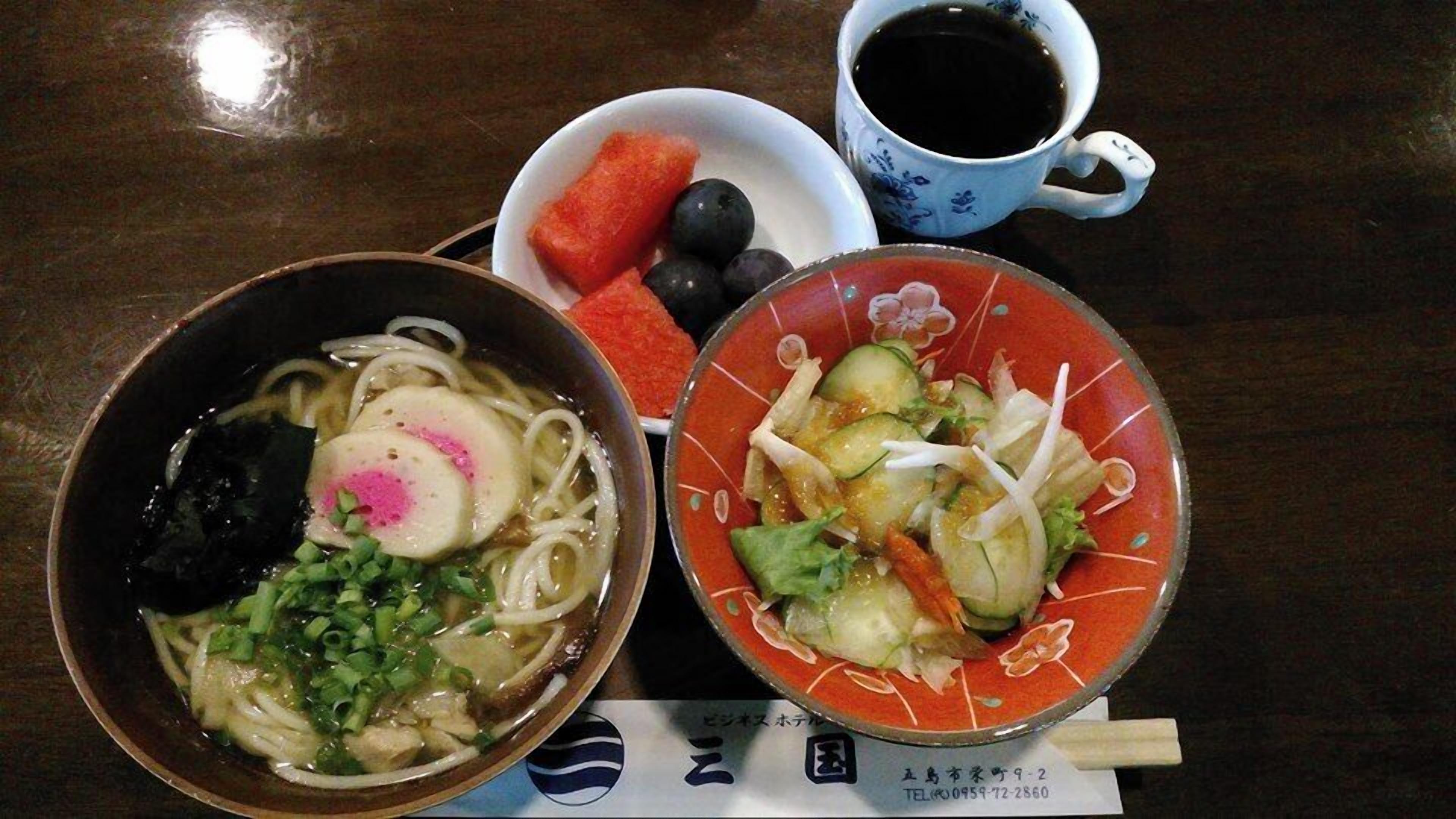 A meal with a bowl of noodles topped with a pink egg, a bowl of salad with cucumber and lettuce, and a cup of black tea.