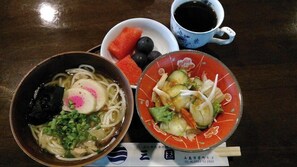 A meal with a bowl of noodles topped with a pink egg, a bowl of salad with cucumber and lettuce, and a cup of black tea. - Business Hotel Mikuni (Goto)