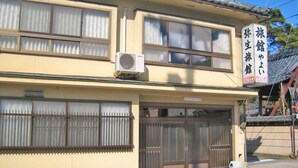 A two-story building with a traditional Japanese architectural style, featuring sliding doors and a tiled roof. - Yayoi Ryokan (Ono)